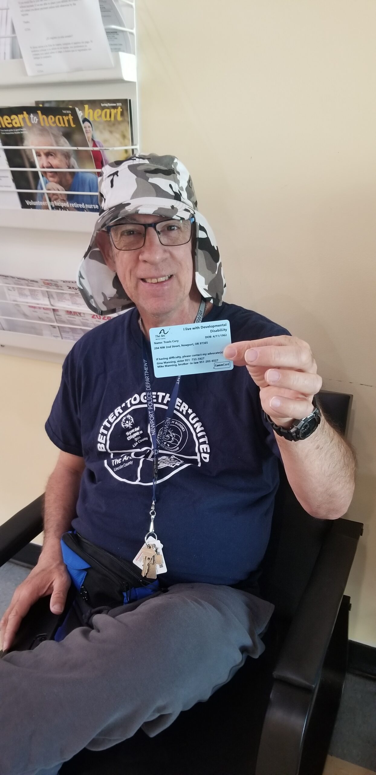 Travis, a man wearing jeans, T-shirt, lanyard, and a hat, shows his CommCard